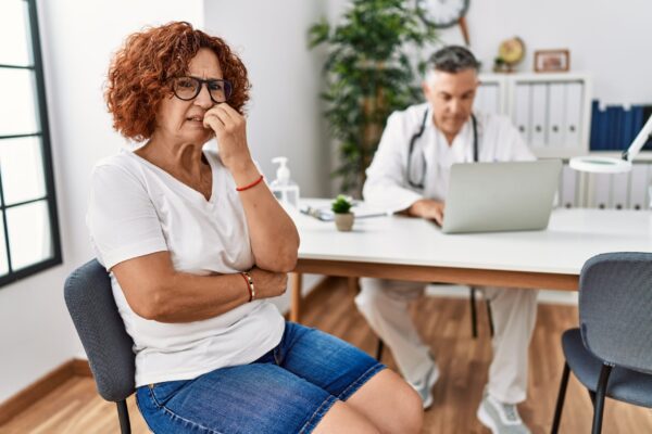 Woman sitting at doctor appointment looking stressed and nervous with hands on mouth biting nails. anxiety problem.